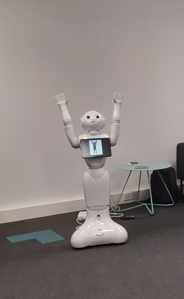 Kuvassa robotti ohjaa nostamaan kädet ylös.
